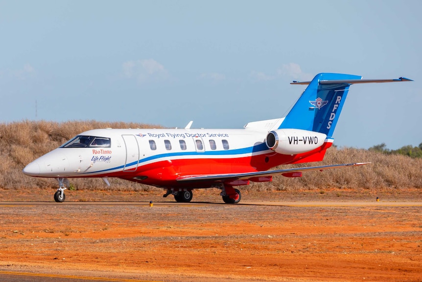 A twin-engine jet in white, red and blue RFDS livery sits on a red-dirt runway