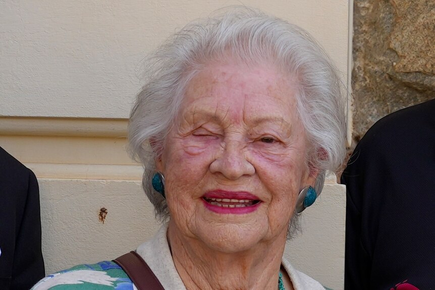 An elderly woman with white hair wearing a floral shirt smiles