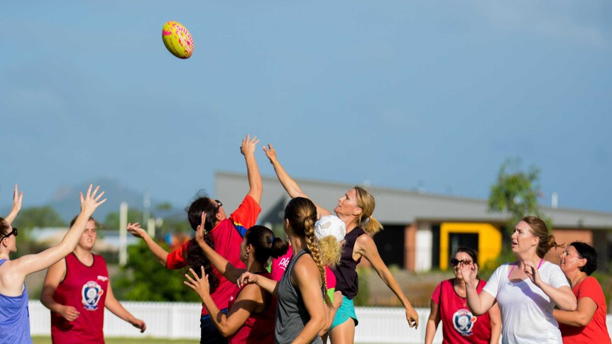 A group of women playing AFL, jumping for a ball in the air.