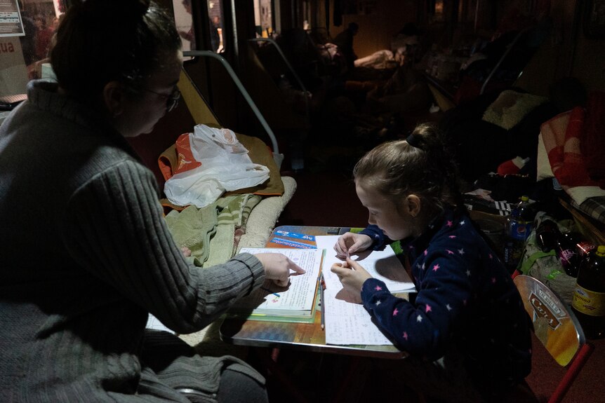A woman points to a small girl's notebook on a table 
