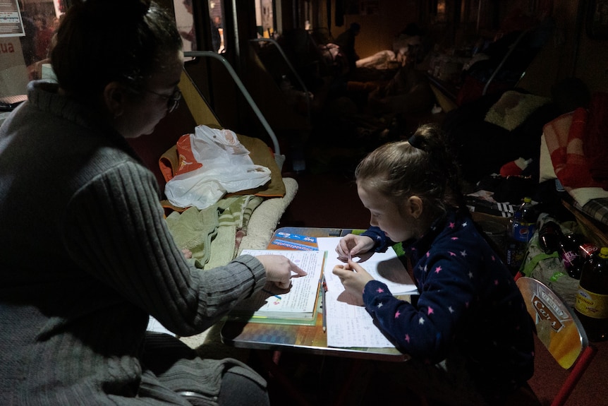 A woman points to a small girl's notebook on a table 