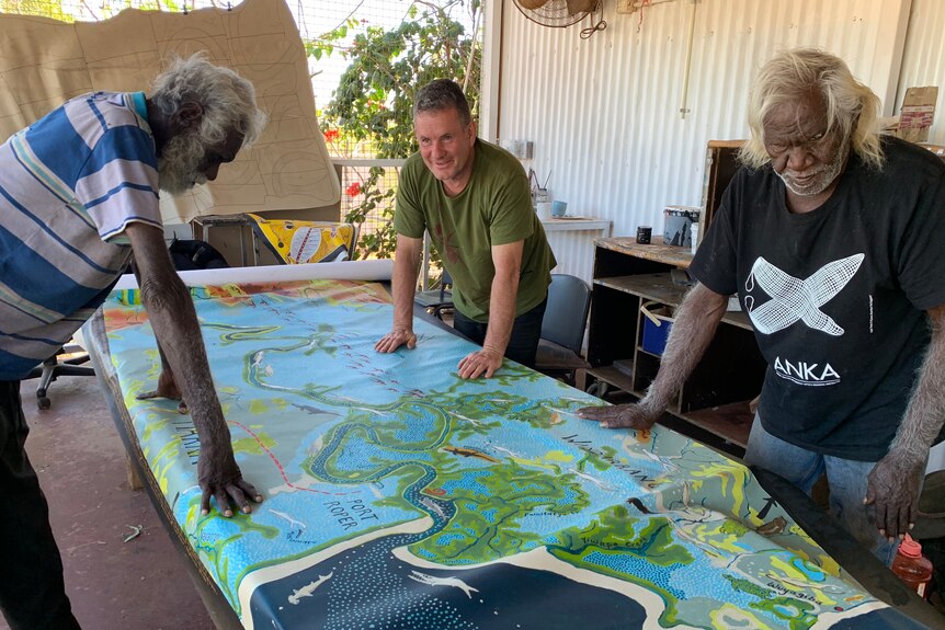 dos hombres aborígenes mirando un mapa pintado de colores con otro hombre