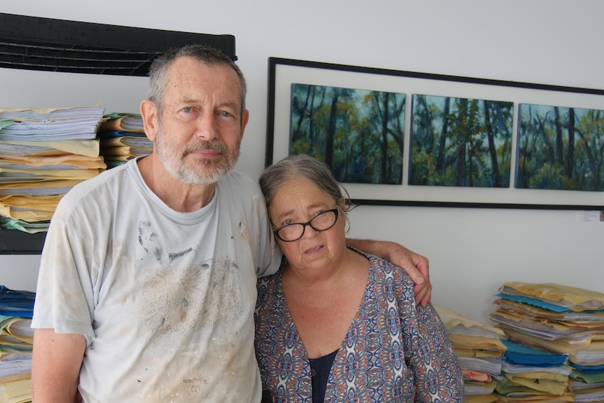 An older man and woman looking sad with lots of wet files behind them