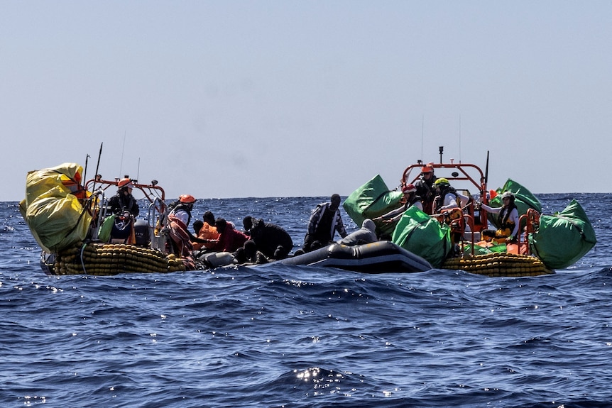 Two rubber boats bob around in open ocean while a third boat helps people off one of them