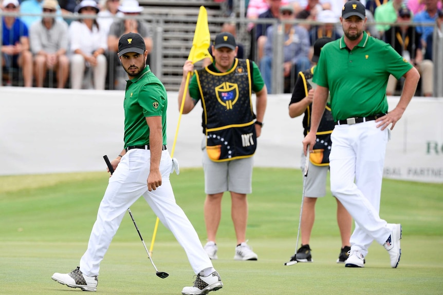 Abraham Ancer looks behind him while walking. Standing on the adjacent green is Marc Leishman.