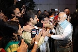 Narendra Modi stands in front of a crowd of people reaching out to touch him.