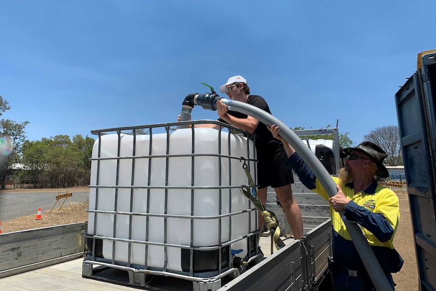 Two men help to fill a large water tank.