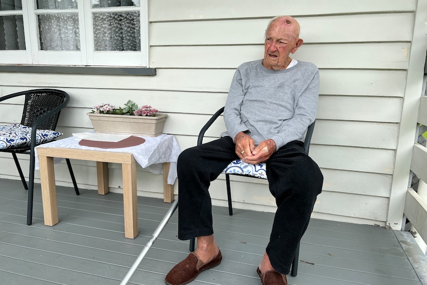 An elderly man sitting on the porch outside his home.