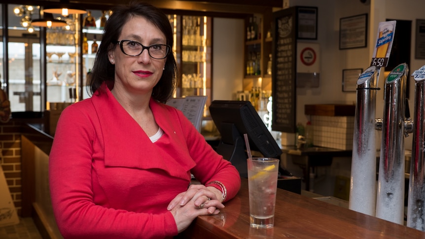 PhD student Sue Sharrad stands at a bar with a glass of water.