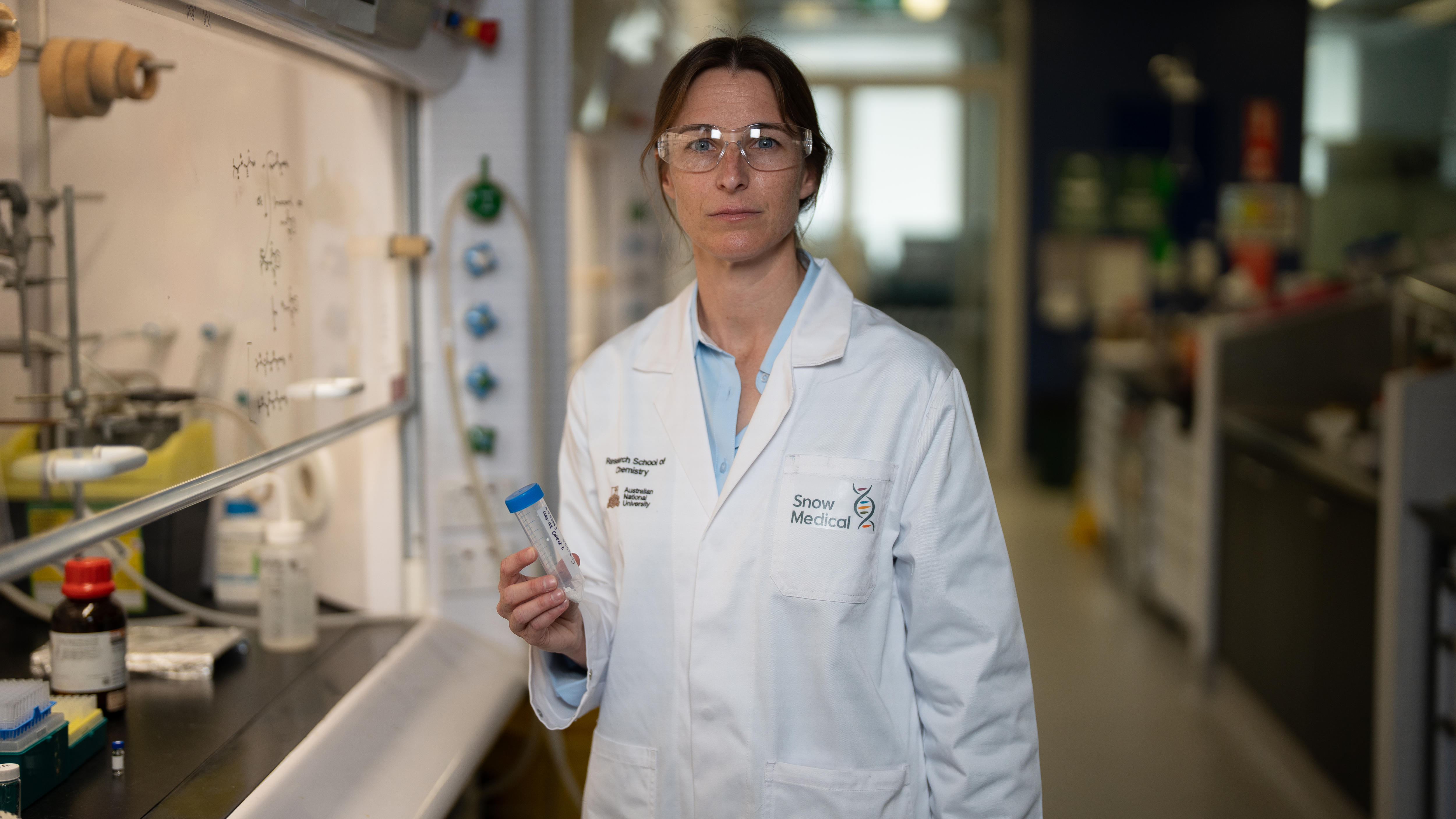 Uma mulher com um jaleco segurando um tubo transparente em um laboratório.
