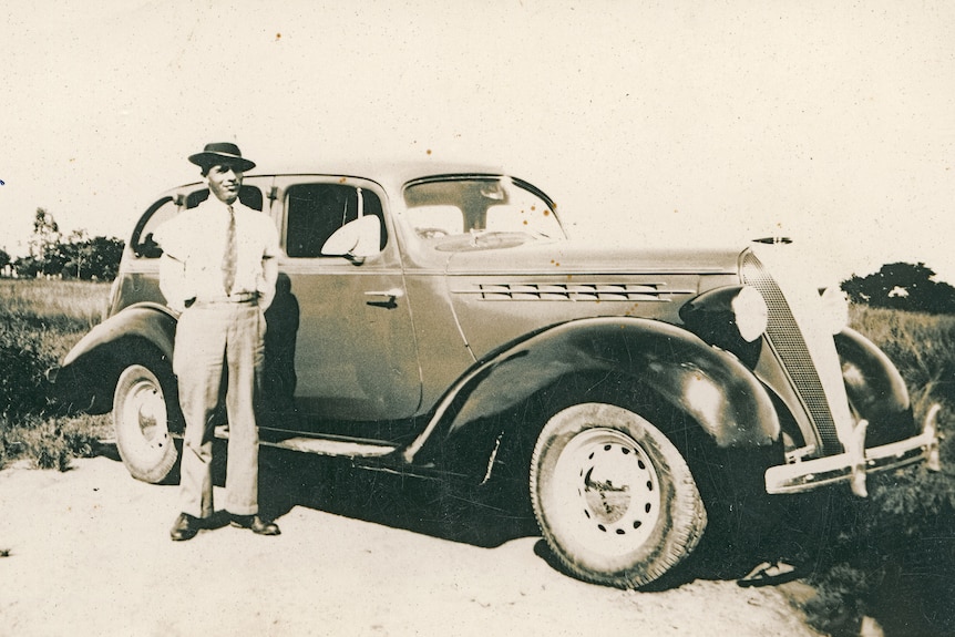 A black and white photo of Mario Strano with his taxi which is a classic car
