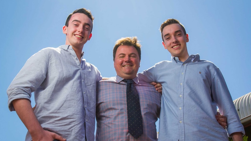 Three men stand with blue sky behind them