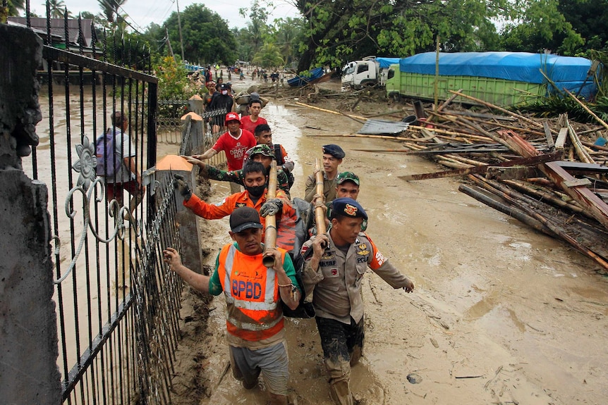 Two lines of rescue workers carry equipment on their shoulders as they walk through flood waters.