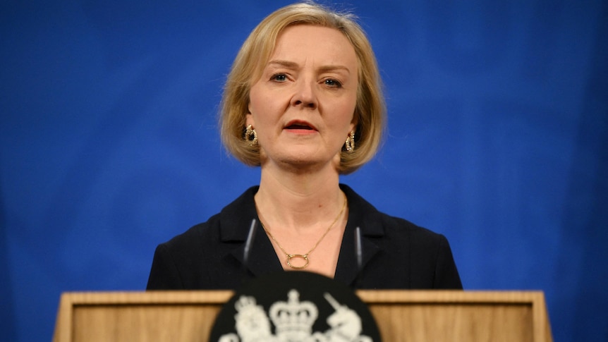 Liz Truss speaks on a podium in front of a blue background.