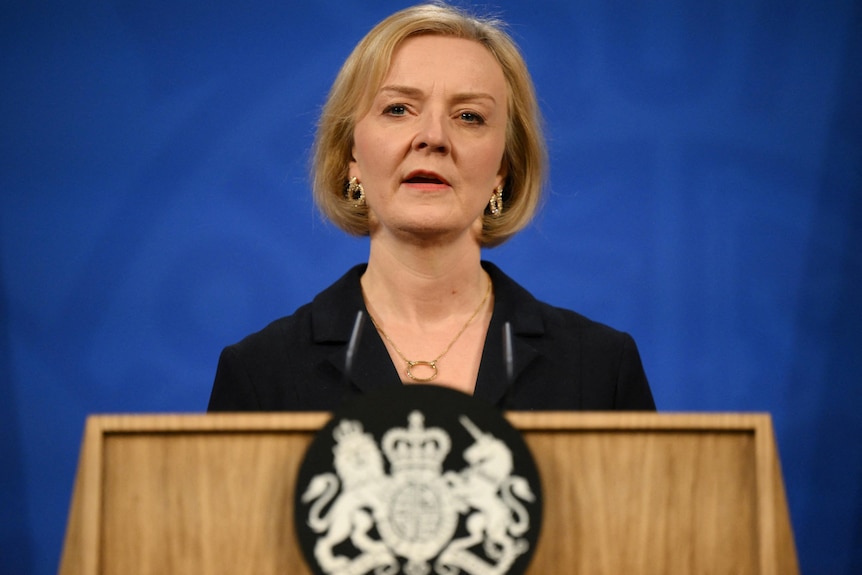 Liz Truss speaks on a podium in front of a blue background.