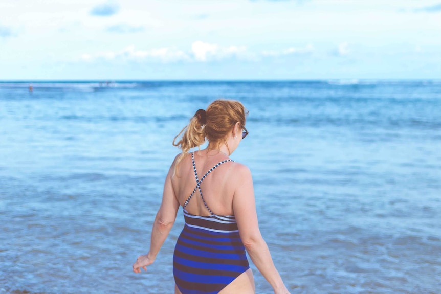A curvy woman wearing a striped swimsuit in the ocean to depict how to make swimwear shopping less stressful.