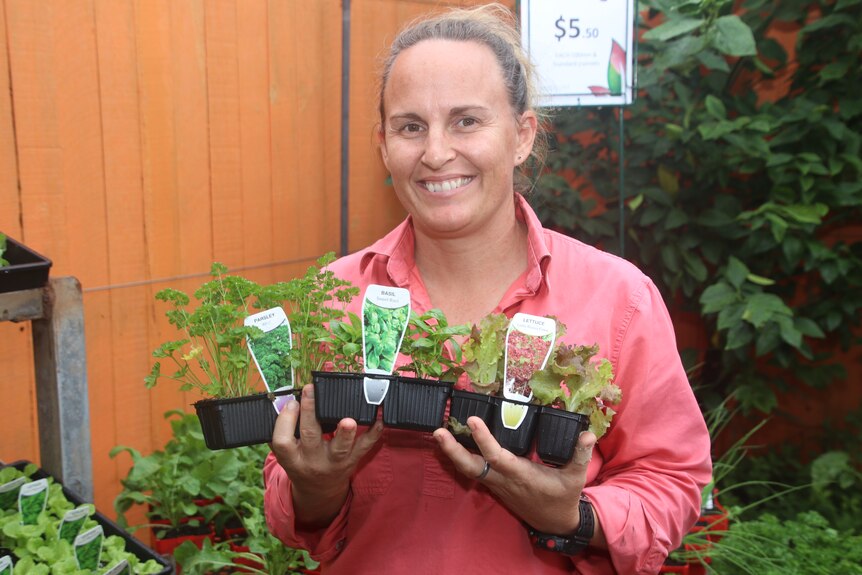 Rebecca in a pink shirt holding three small trays of seedlings
