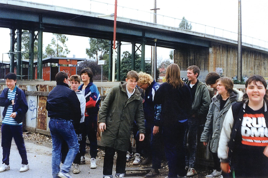 A bunch of teenage boys smiling and hanging about at a railway station