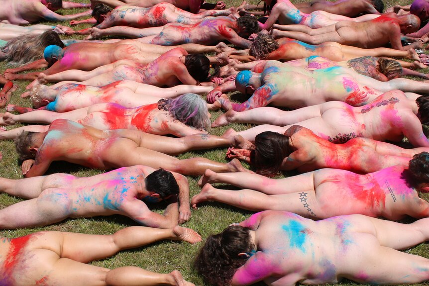 Rows of naked people with coloured dust all over them.