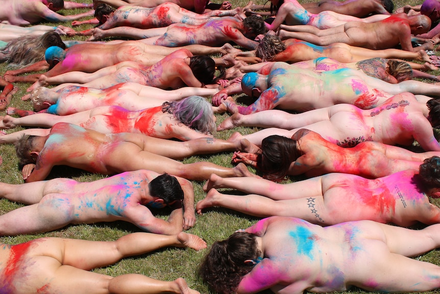 A line of naked people covered in multicolored dust.