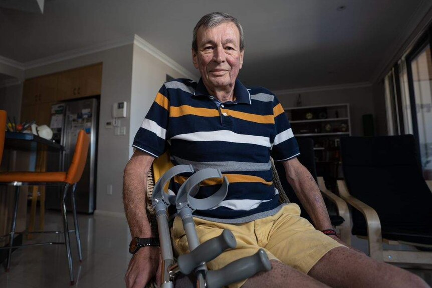 Man sitting in his living room, with crutches propped up against the chair