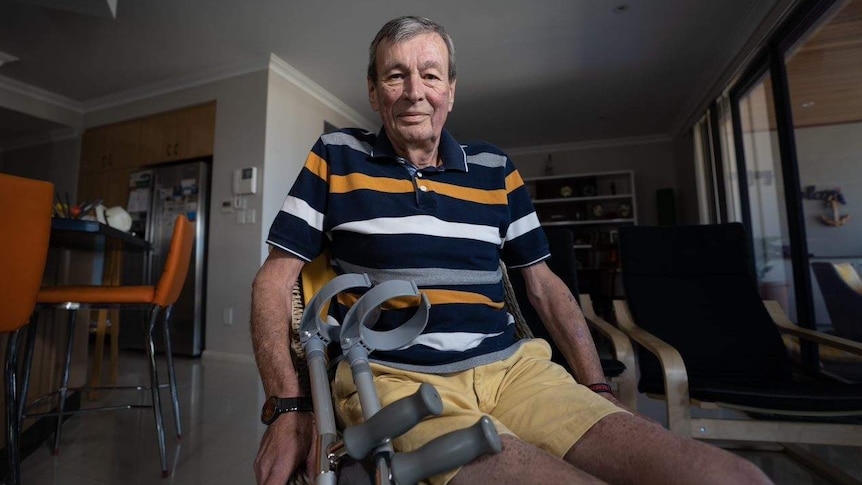 Man sitting in his living room, with crutches propped up against the chair