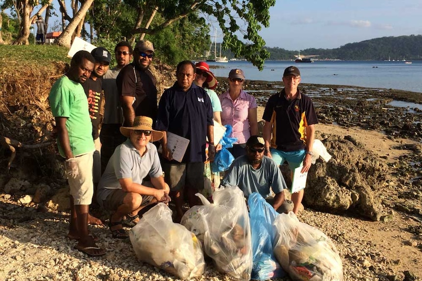 Volunteers gather on a Vanuatu beach with bags of plastic rubbish lined up in front of them.