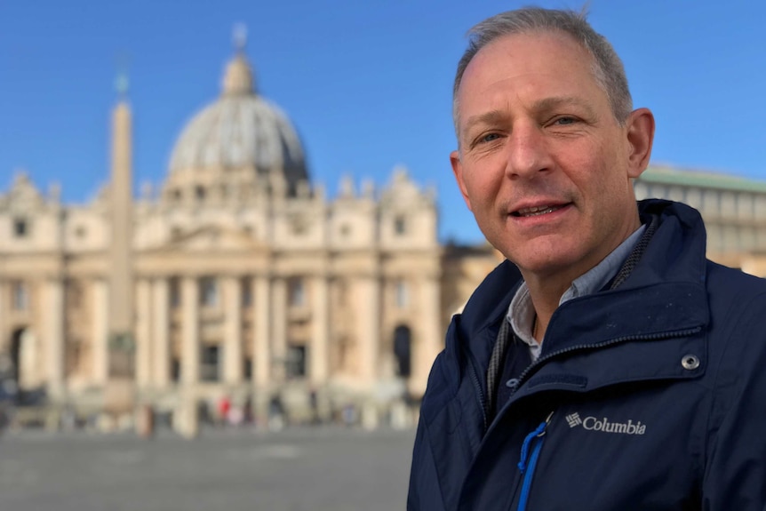 A man in a jacket stands in front of St Peter's Basilica in Rome.