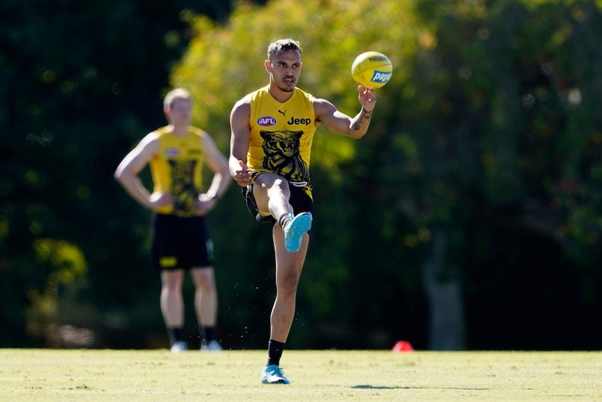 Richmond player Sydney Stack on a football oval kicking a yellow ball.