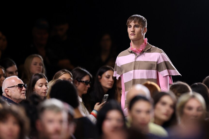 A male model wears a pink and brown polo shirt cut at the sides, with a matching pink longsleeve mesh shirt underneath.
