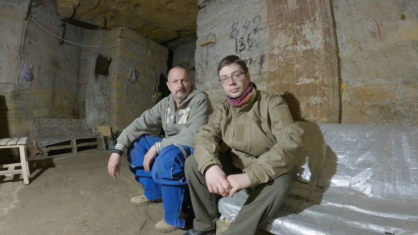 Two men sit in an underground tunnel.