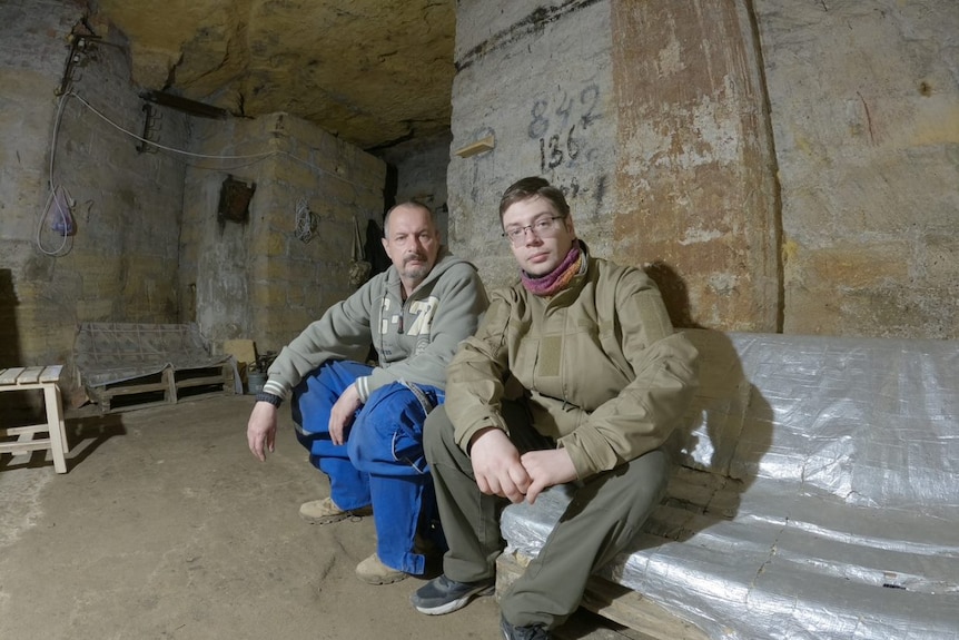 Two men sit in an underground tunnel.