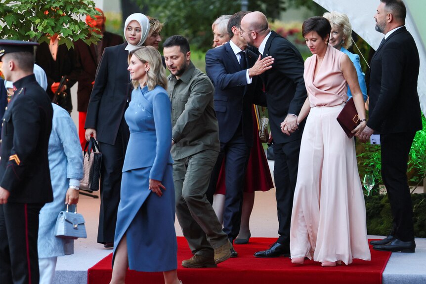 zelenskyy and his wife walk on a red carpet amid other officials in formal dress