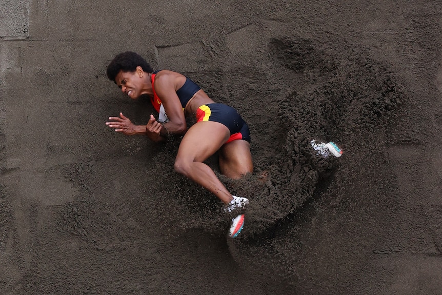 Aerial shot of Rellie Kaputin lying in the sand grimacing after competing in the women's long jump at the Tokyo Olympics