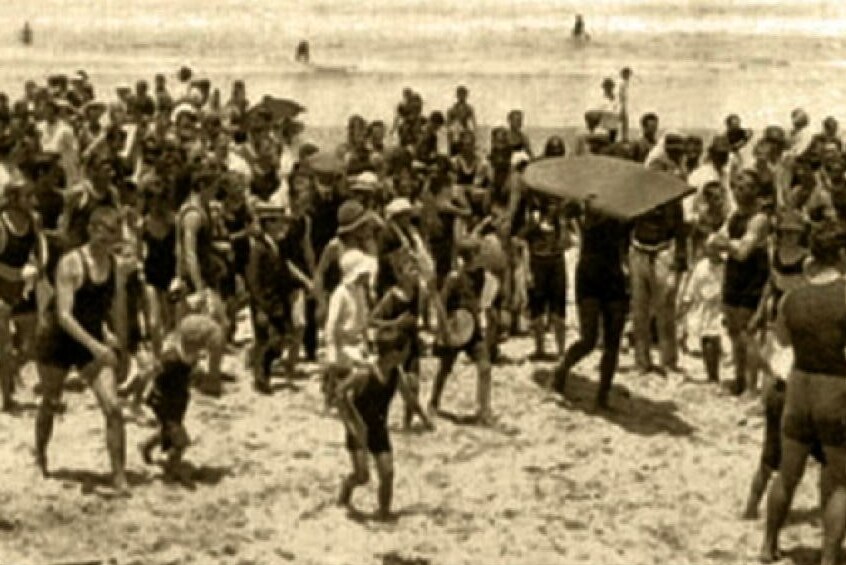 Crowds follow Duke Kahanamoku up Freshwater beach after his surfing exhibition in January 1915