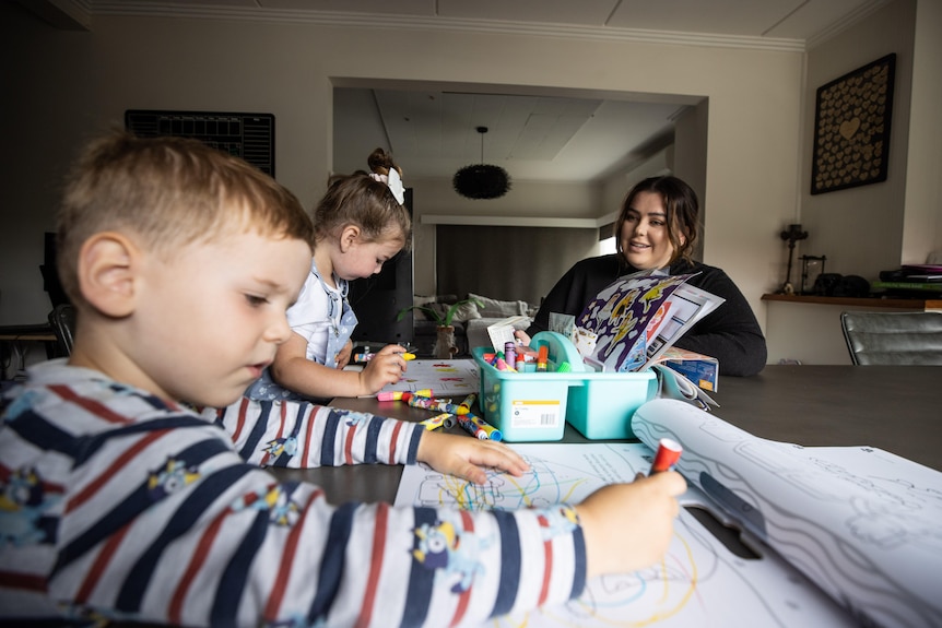 A woman and two children do craft at a table.