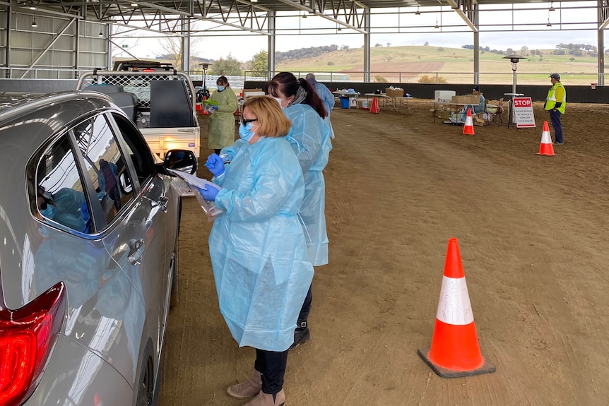 Health staff in personal protective equipment speaking to people in cars 