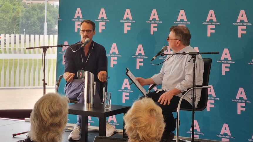 Christian Spuck (left) and Michael Cathcart (right) sit at microphones on a stage in front of an Adelaide Festival banner.