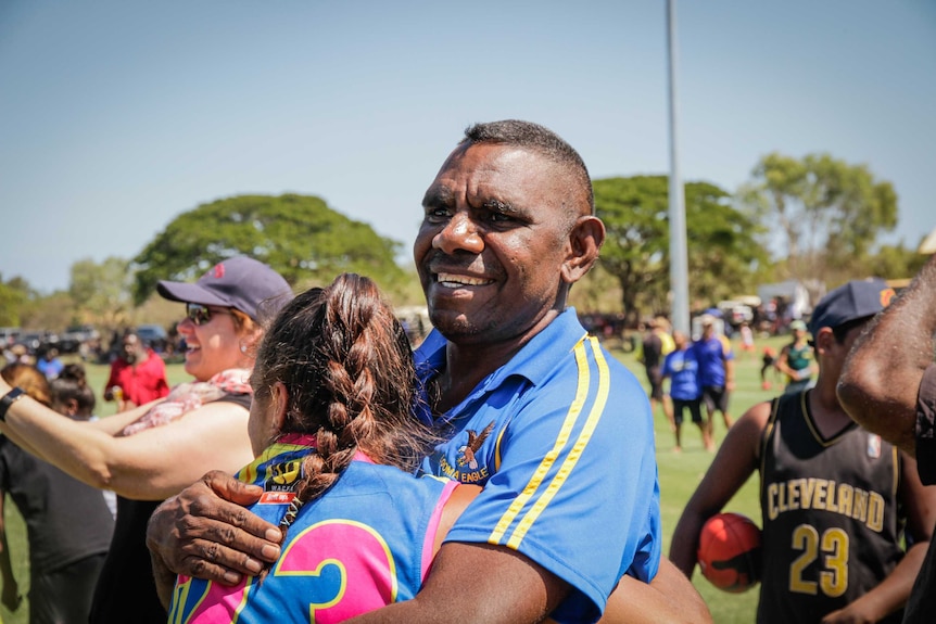 An Indigenous man and girl hugging in a crowd on a football field.