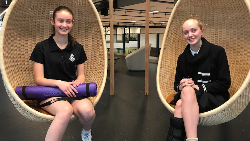 students in uniform hold a yoga mat and sit in eff shaped hanging chairs