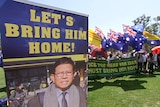 A poster reads: 'let's bring him home' as people stand in the background with Australian flags.