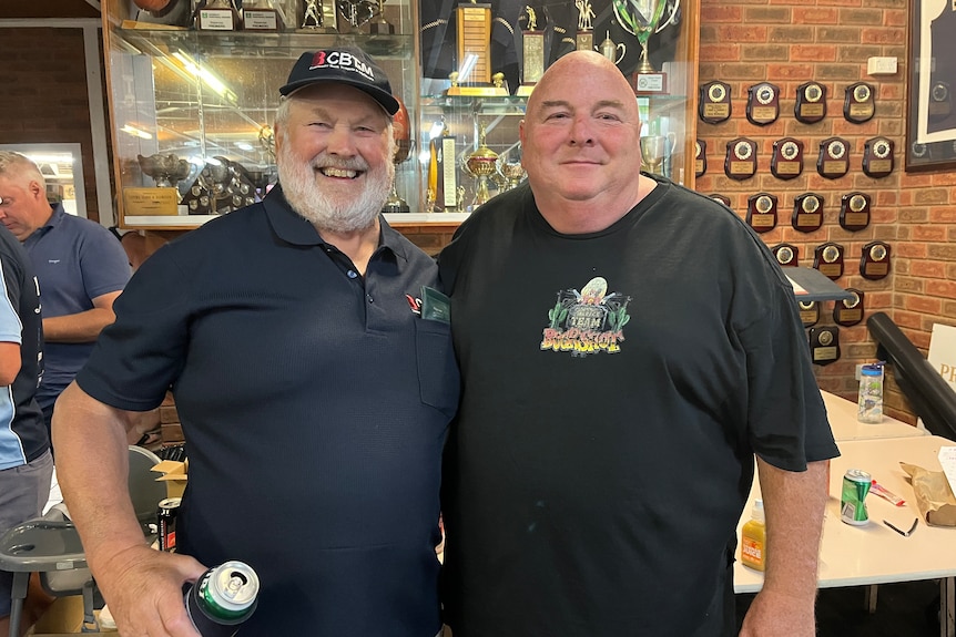 Two men standing beside each other with a number of sports medals on display behind them