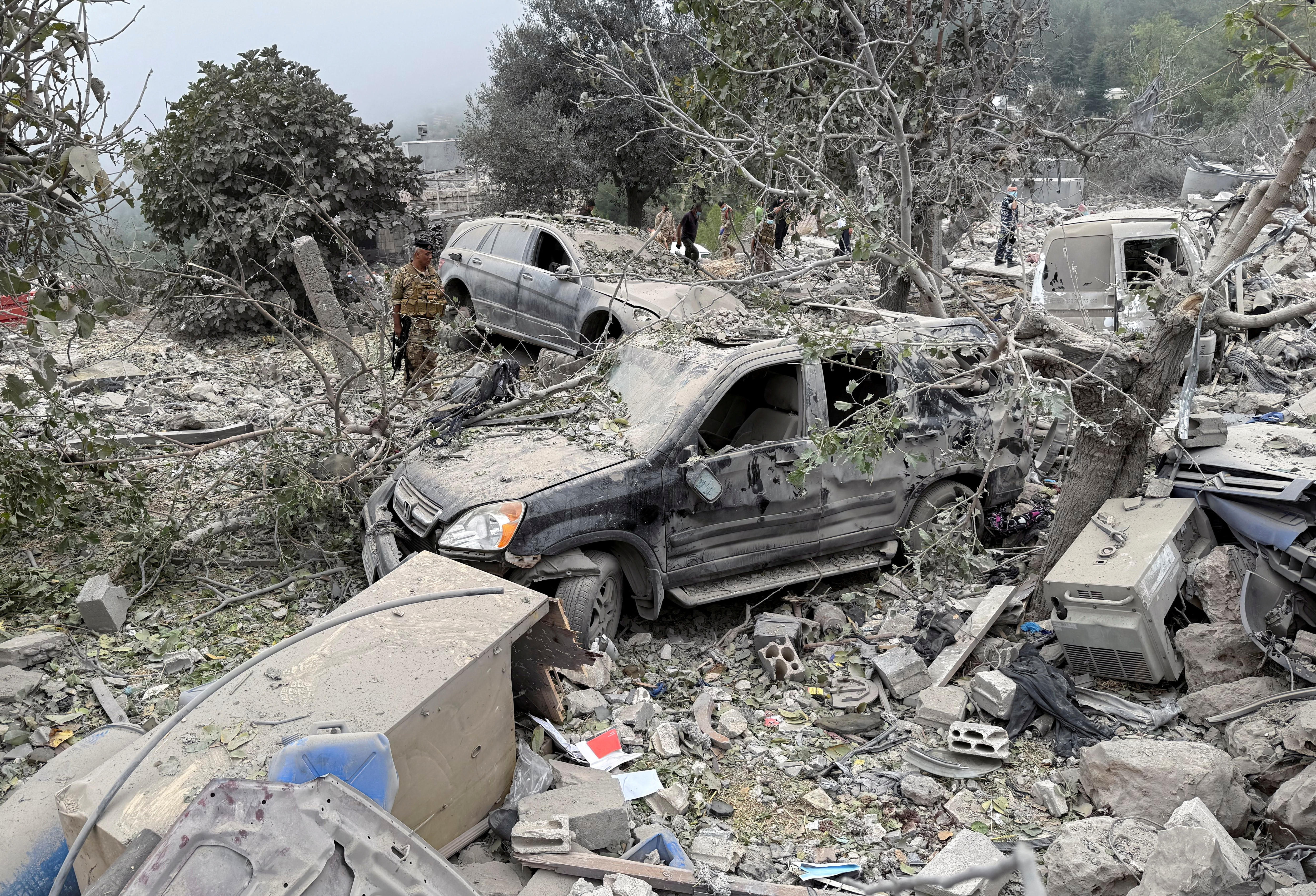 Three cars stand covered by trees and dust in the aftermath of a blast