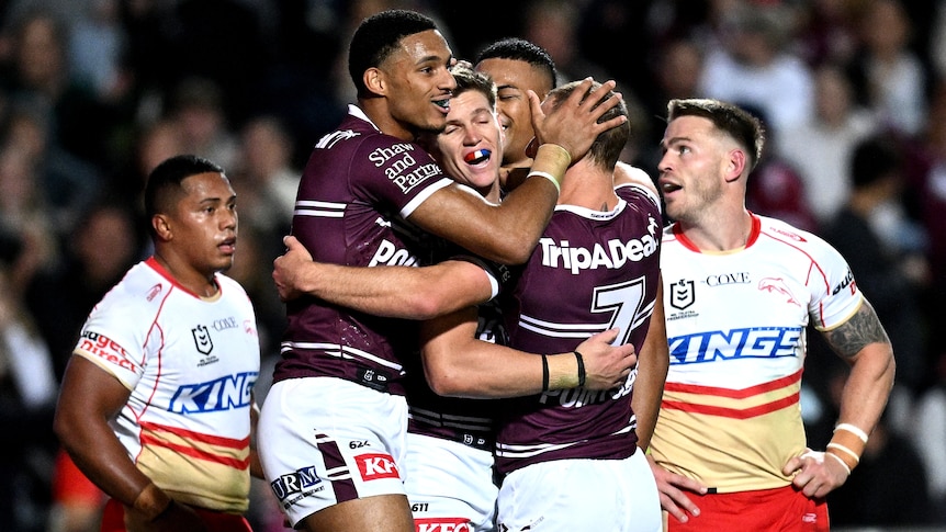 Four Manly NRL players embrace as they celebrate a try against the Dolphins.