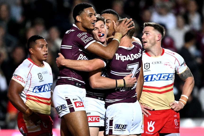 Four Manly NRL players embrace as they celebrate a try against the Dolphins.