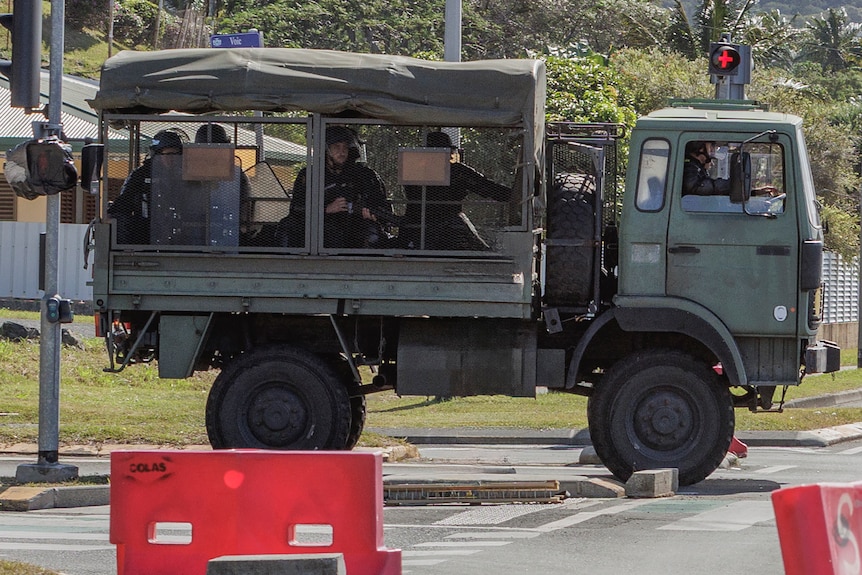 French Gendarmes holding weapons sit in the back of a green truck enclosed in mesh