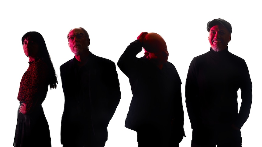 Four people (Pixies) are standing in front of a white background. Their faces are lit in red and their bodies are in shadow.