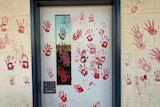 Blood red painted hand prints on a cream cinder block wall and white door