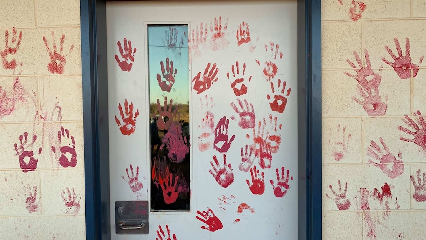 Blood red painted hand prints on a cream cinder block wall and white door