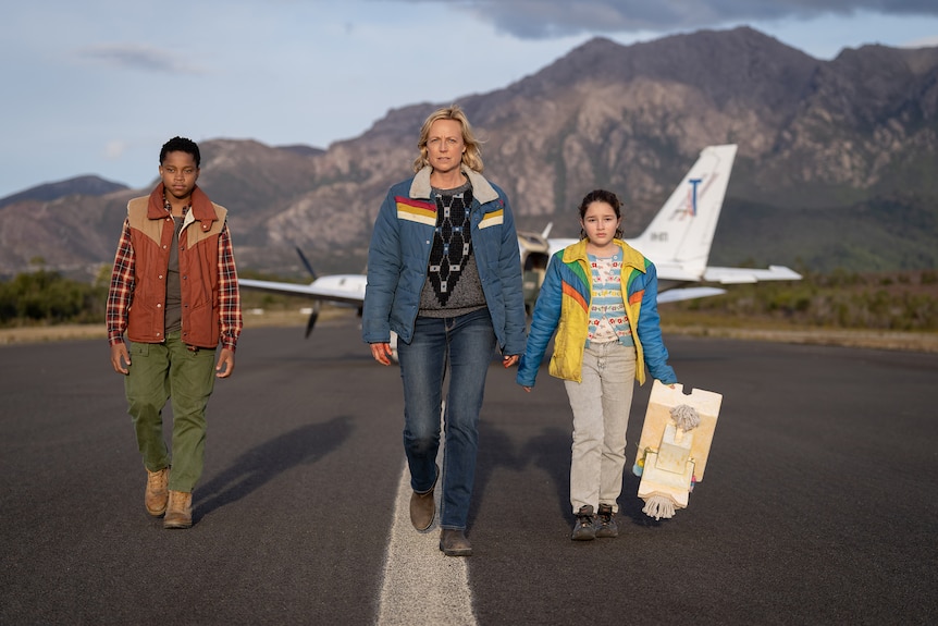 A woman and two children walk down a runway with an small plane behind them.